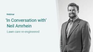 Webinar titled 'In Conversation with Neil Amrhein: Lawn care re-engineered.' The image shows Neil Amrhein, a man with a beard and short hair, wearing a suit jacket over a button-down shirt, standing and smiling against a light-colored background.