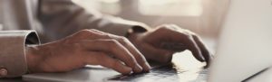 Close-up photograph of hands typing on a laptop keyboard, with soft, natural light filtering through a window in the background.